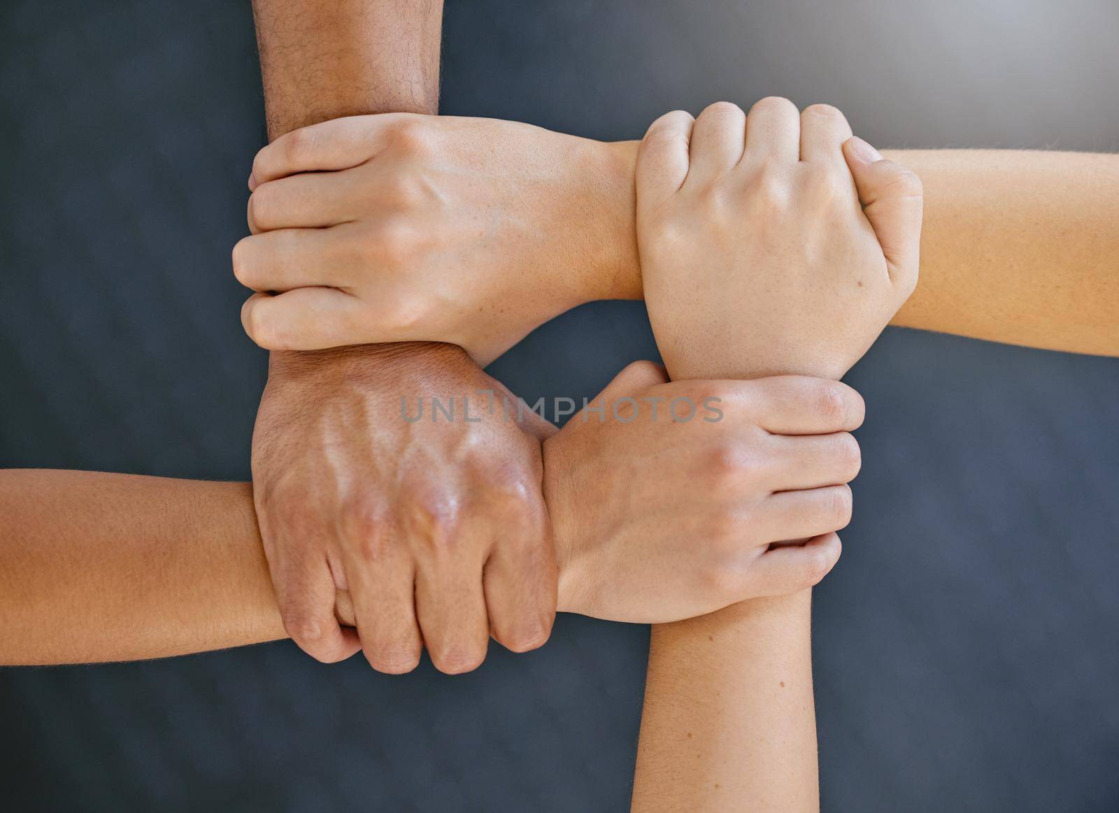 Closeup of diverse group of people from above holding each others wrists in a circle to express unity, support and solidarity. Connected hands of multiracial community linked for teamwork in a huddle. Society join together for collaboration and equality.