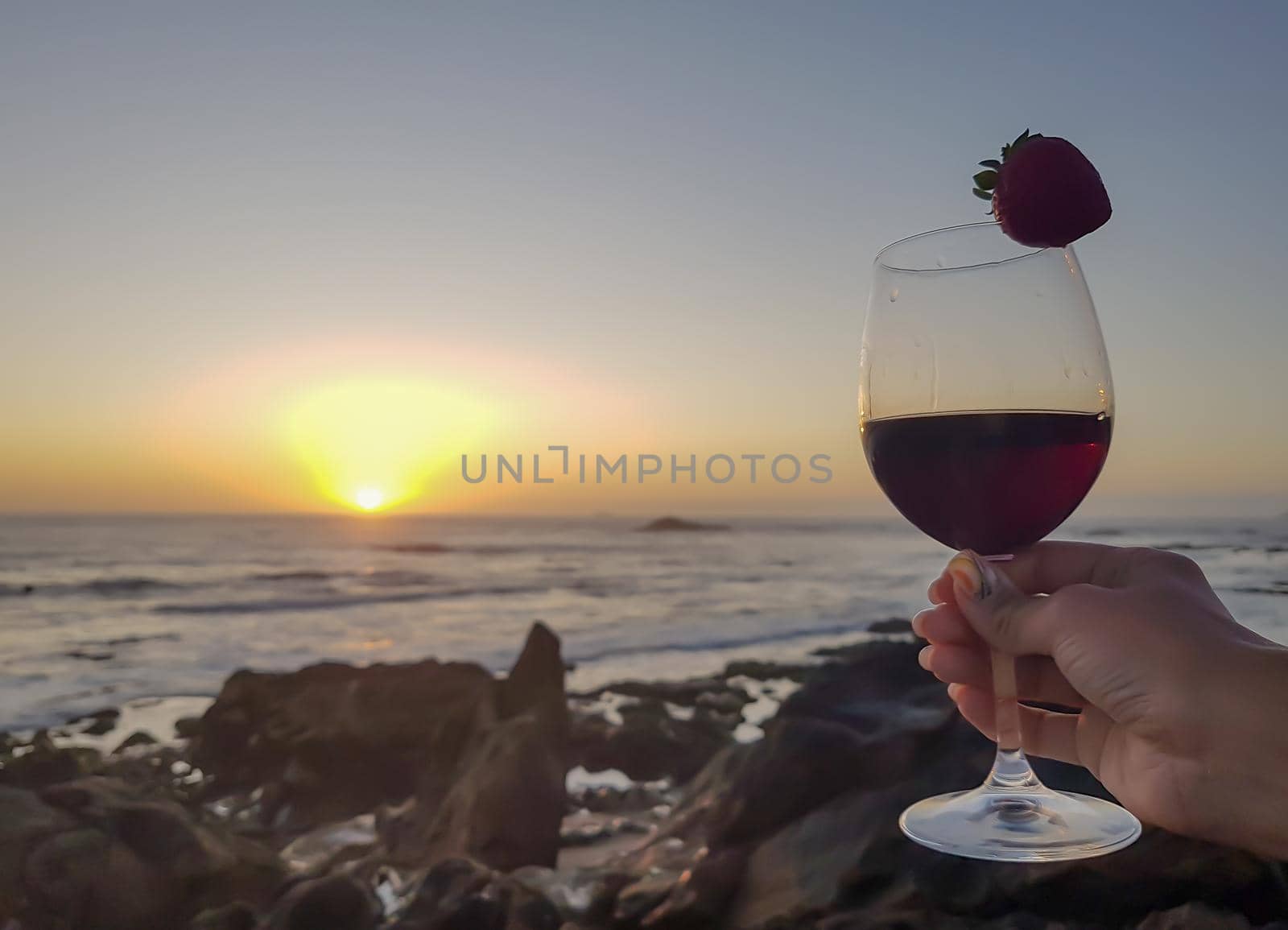 woman with glass of red wine and strawberry on the beach. Sunset wonderful time by igor010