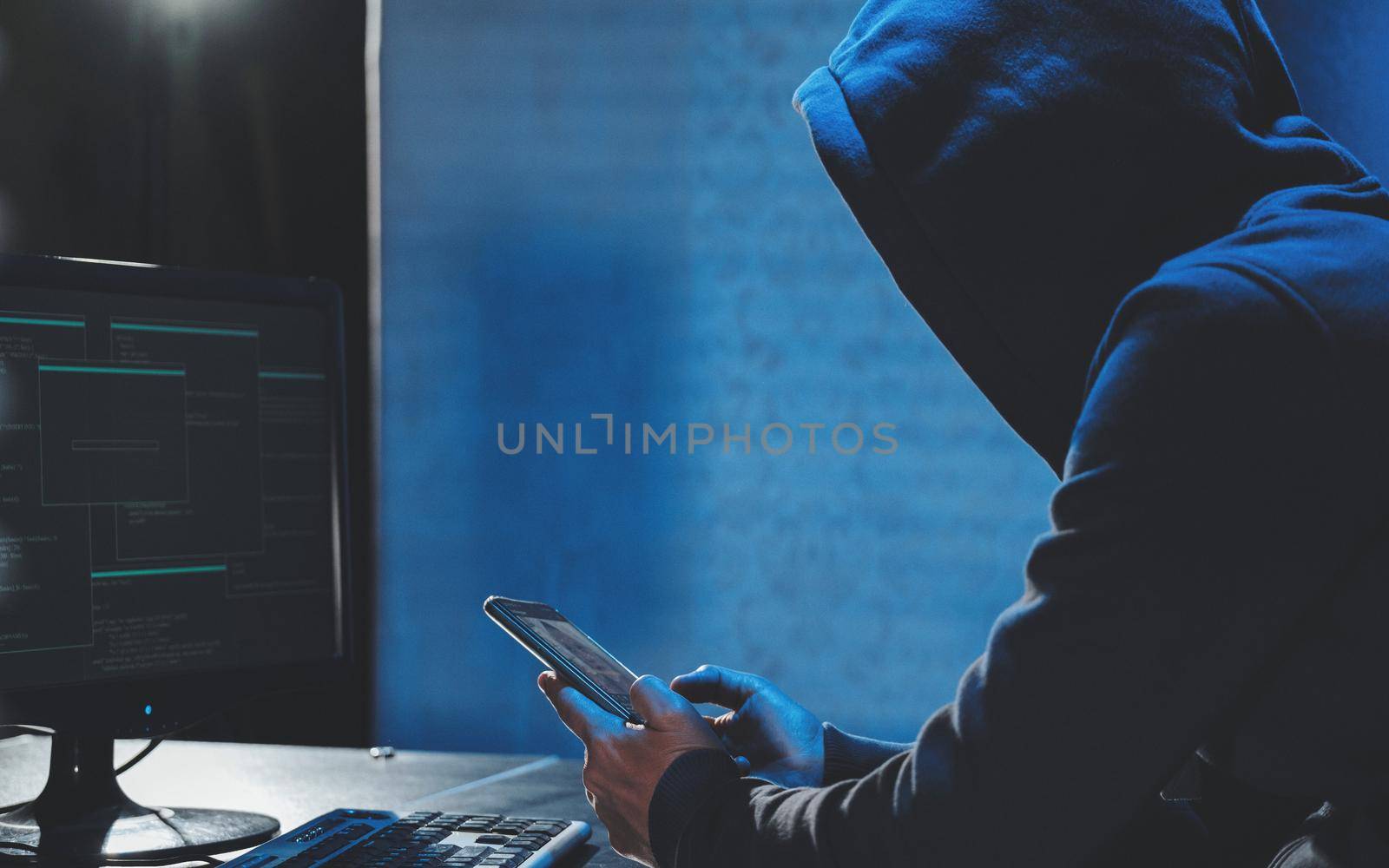 Overhead hacker in hood working at computer and mobile phone typing text in dark room, An anonymous hacker uses malware with mobile phone to hack password, personal data steals money from bank. cyber by igor010