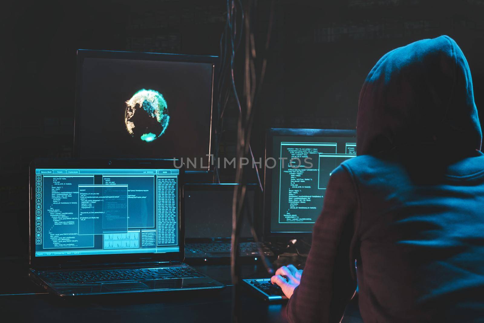 Back hooded hacker using malicious software hack corporate data center. malefactor hidden underground in dark place, multiple displays with phishing code and global map attack. Download photo