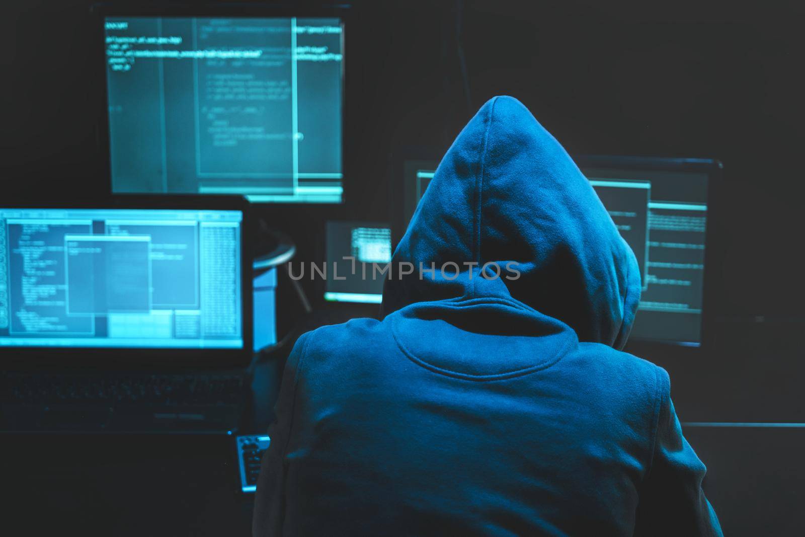 Hacker using computer for organizing massive data breach attack on goverment servers. Hacker in dark room surrounded computers. Download photo