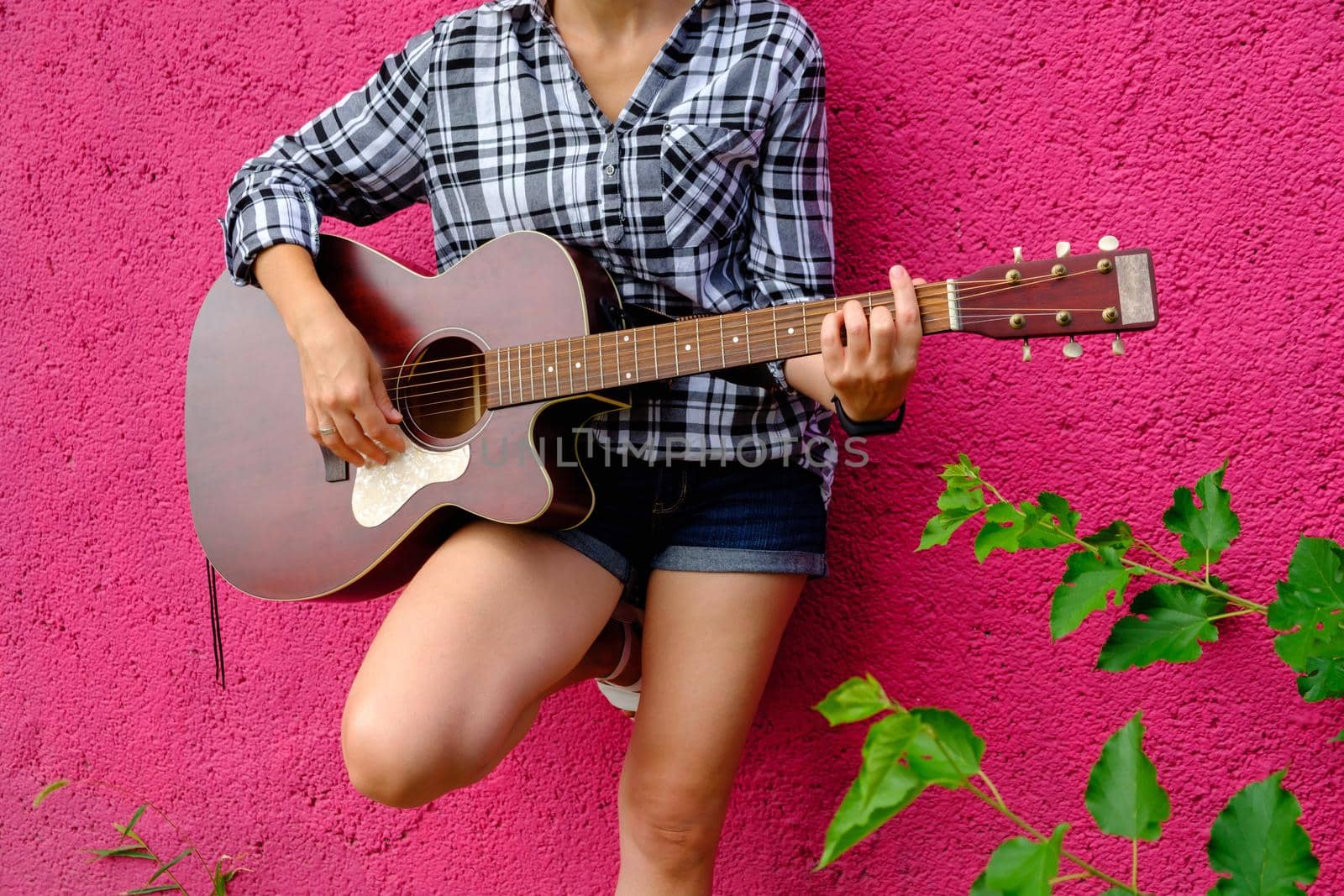 Beautiful girl plays the acoustic guitar. Guitarist on a pink background. Handsome young acoustic guitar blues player performing his musical skills.