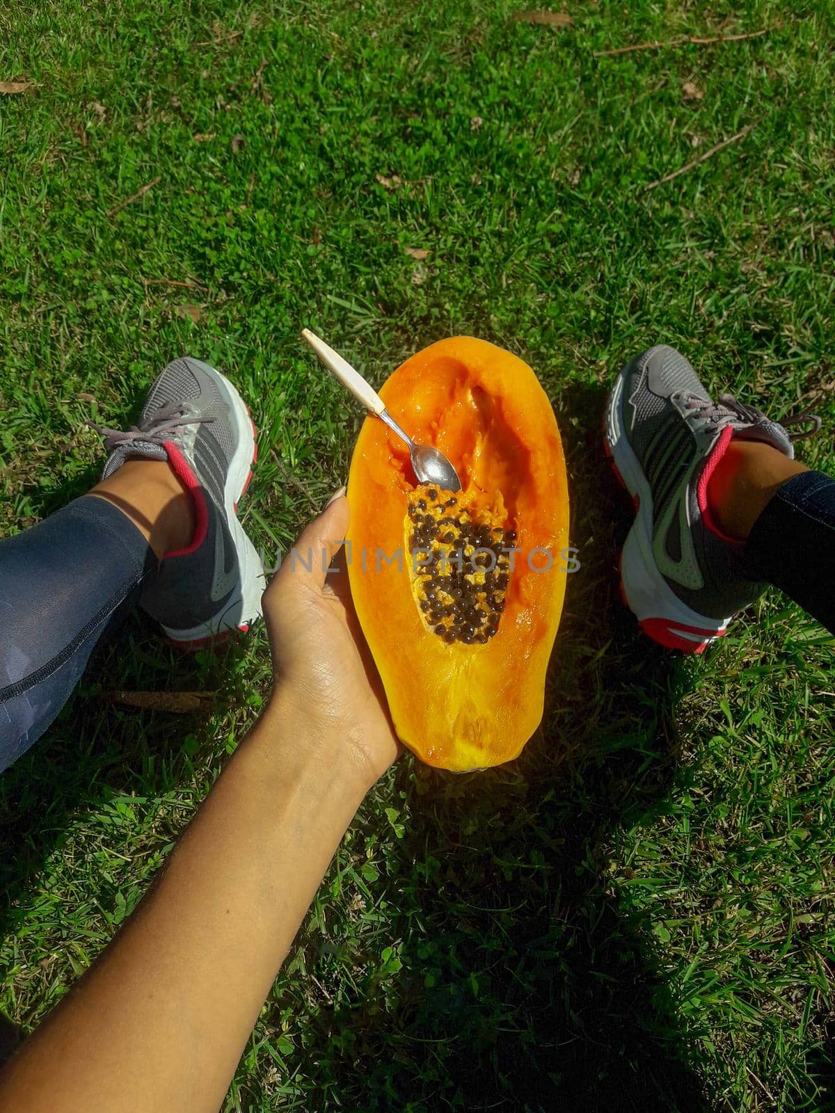 girl sits on a lawn and holds a half of delicious papaya with a spoon. download photo