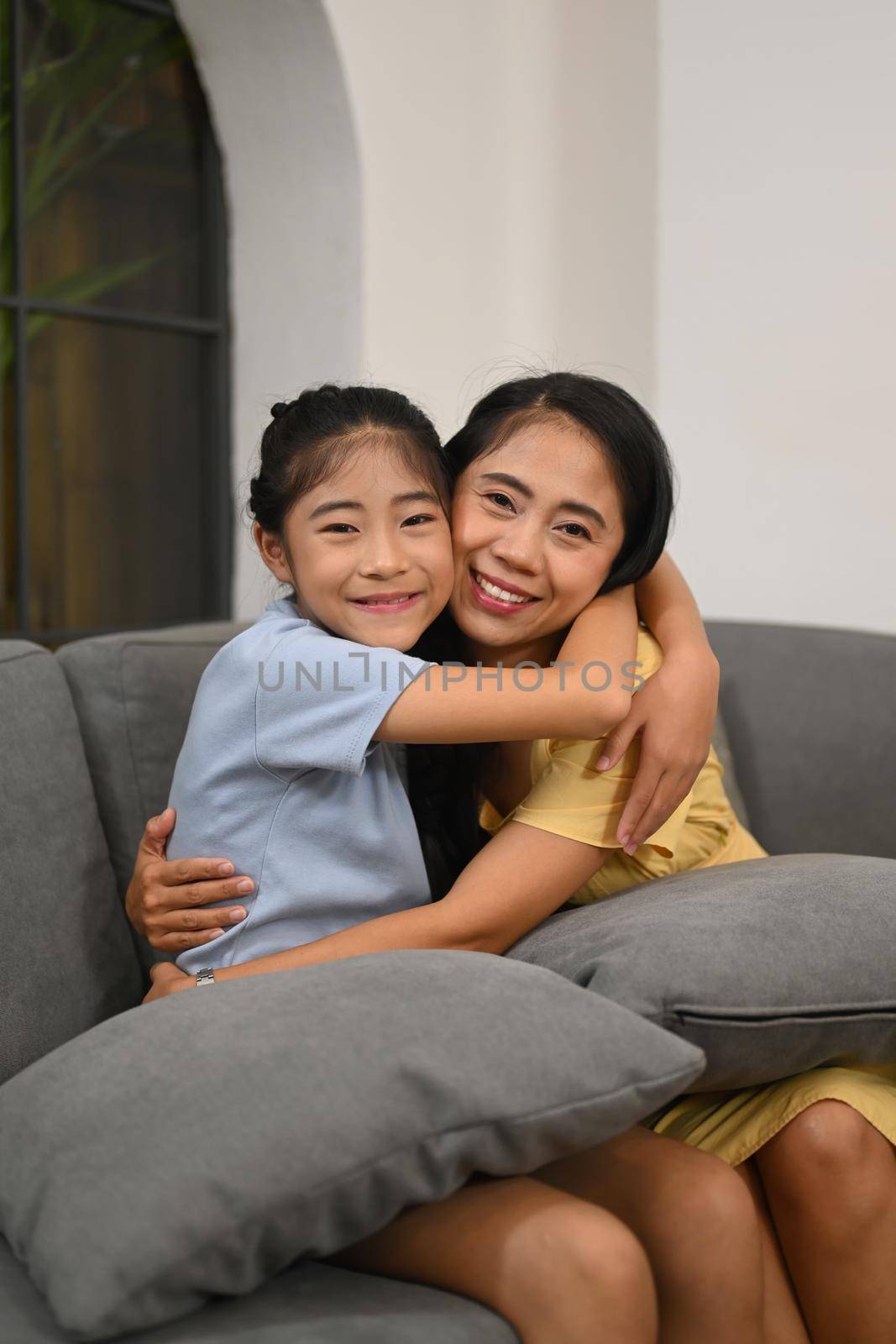 Adorable asian child cuddling mother and smiling at camera. Love and support in family relationships concept.