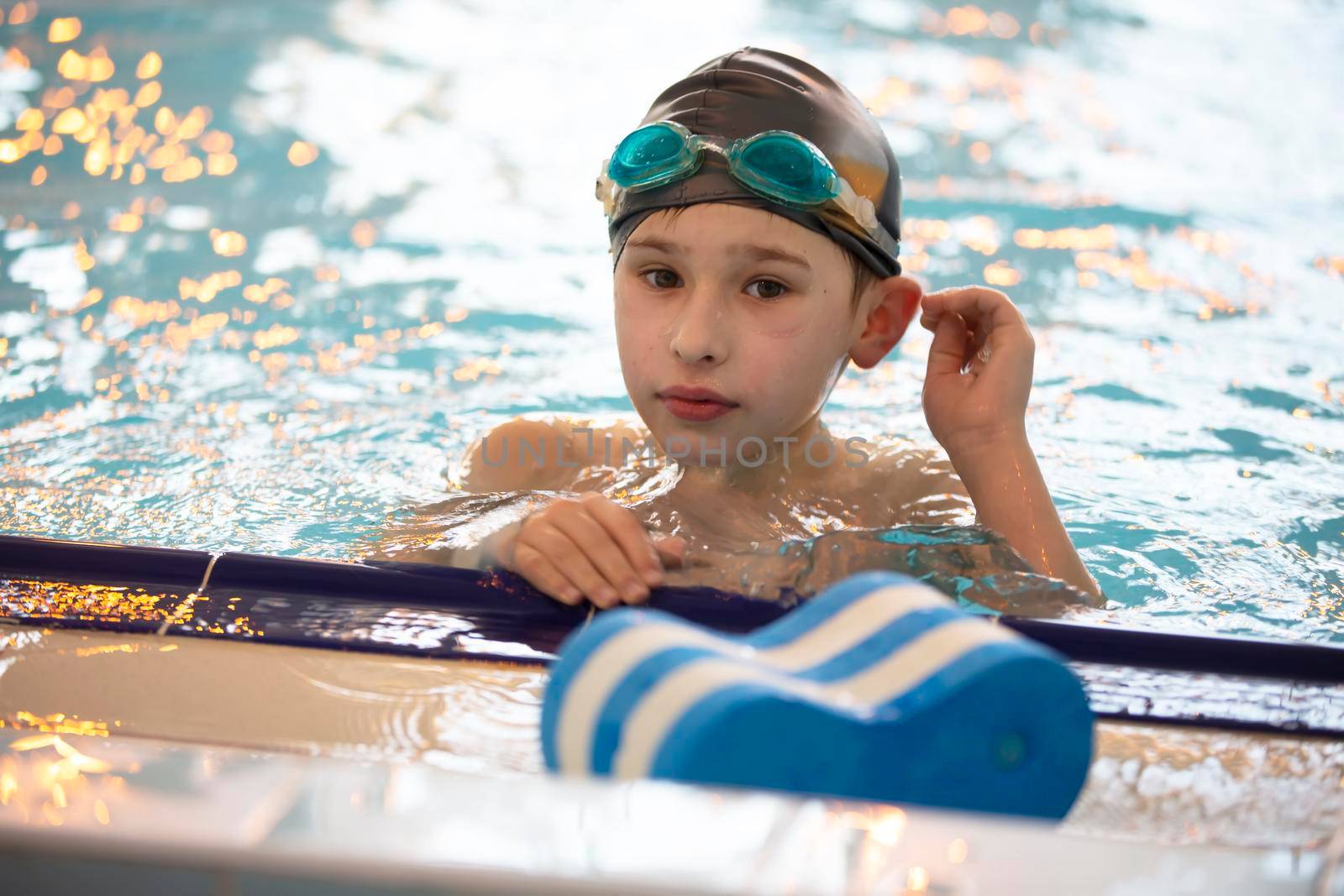 Boy in a swimming cap and swimming goggles in the pool. The child is engaged in the swimming section.