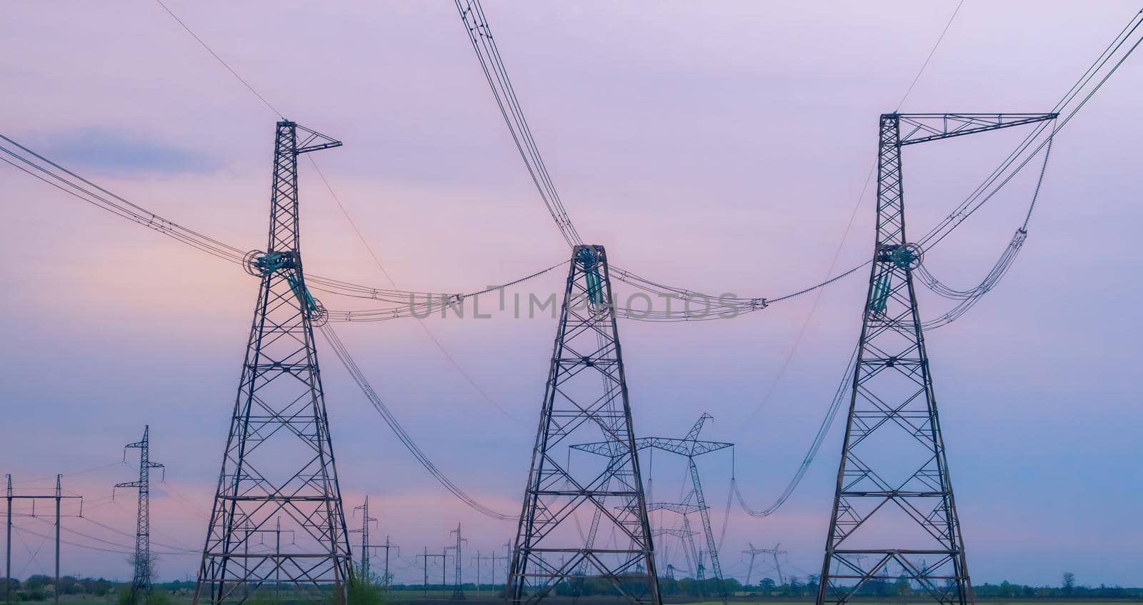 Industrial background group silhouette of transmission towers or power tower, electricity pylon, steel lattice tower at purplr sunset. Texture of high voltage pillar, overhead power line at dusk by igor010