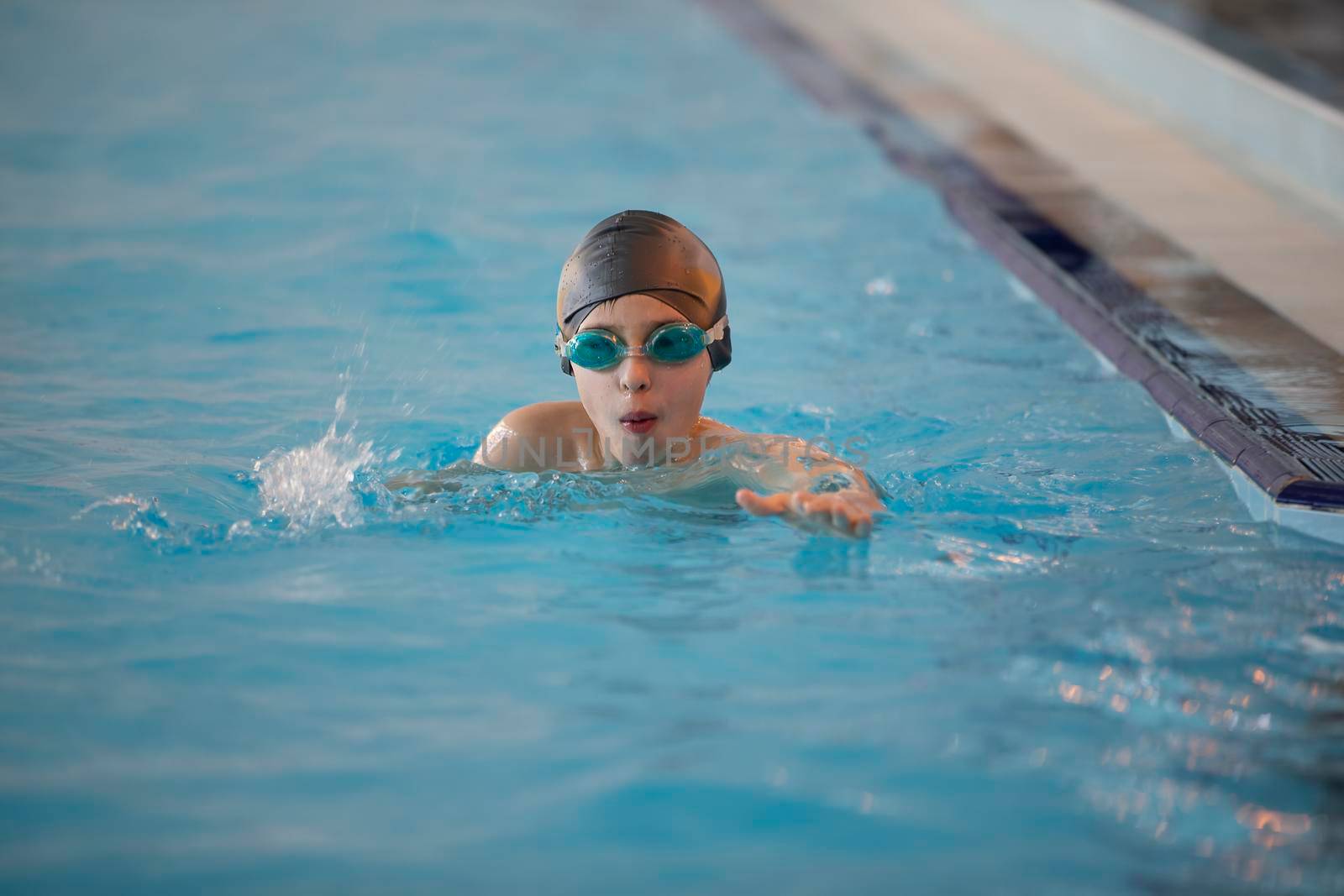 Boy in a swimming cap and swimming goggles in the pool. The child is engaged in the swimming section.