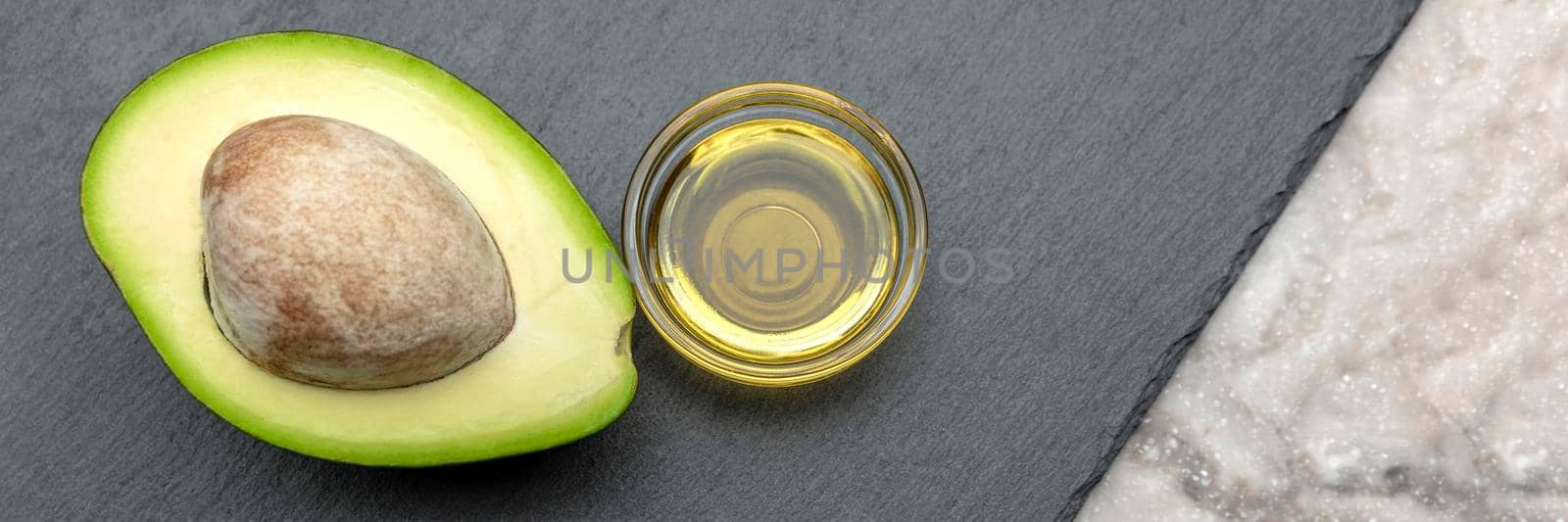 Avocado oil. An avocado with a bone lies on a stone tray. Avocodo oil is poured into a plate. Banner for print, label design, healthy food