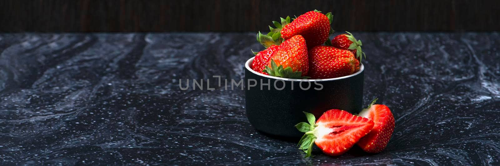 Strawberries on black marble. Ripe strawberries in a saucer on a black background. Place to insert text.