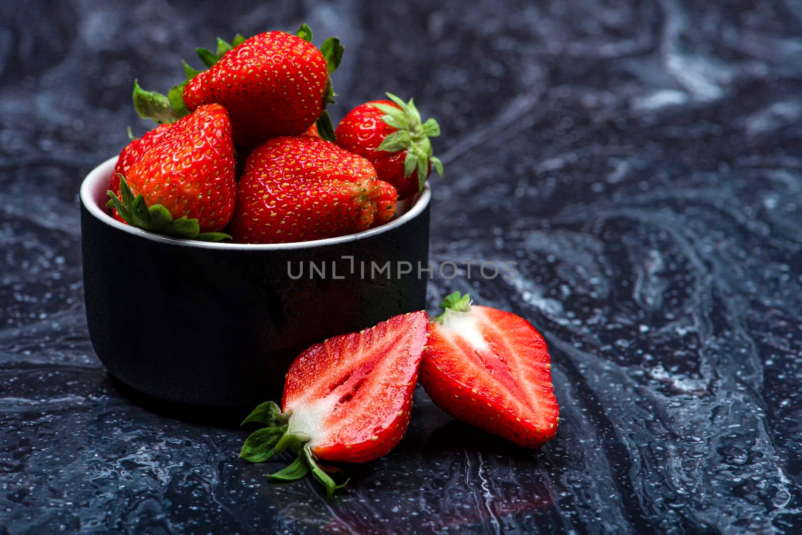 Strawberries on black marble. Ripe strawberries in a saucer on a black background. Place to insert text.