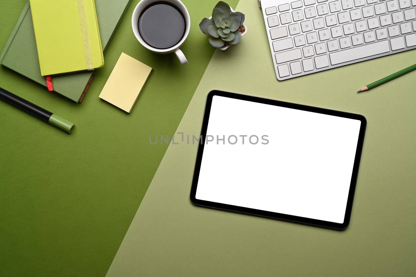 Top view digital tablet with empty screen and supplies on green background.