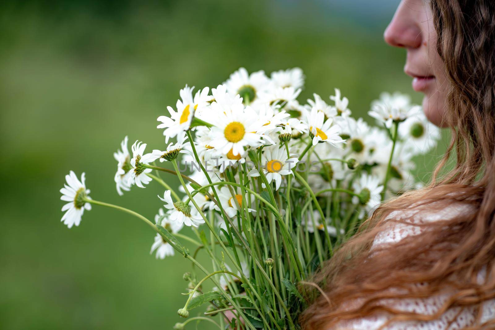 A middle-aged woman holds a large bouquet of daisies in her hands. Wildflowers for congratulations.