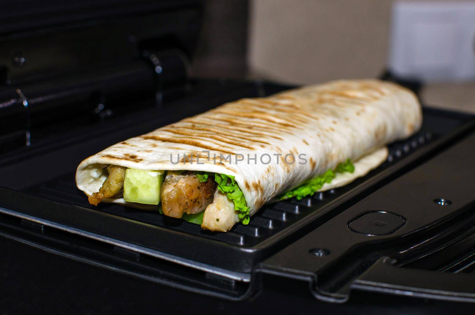 Roll of pita bread, vegetables and chicken. Cooking on an electric grill. Kebab, shawarma