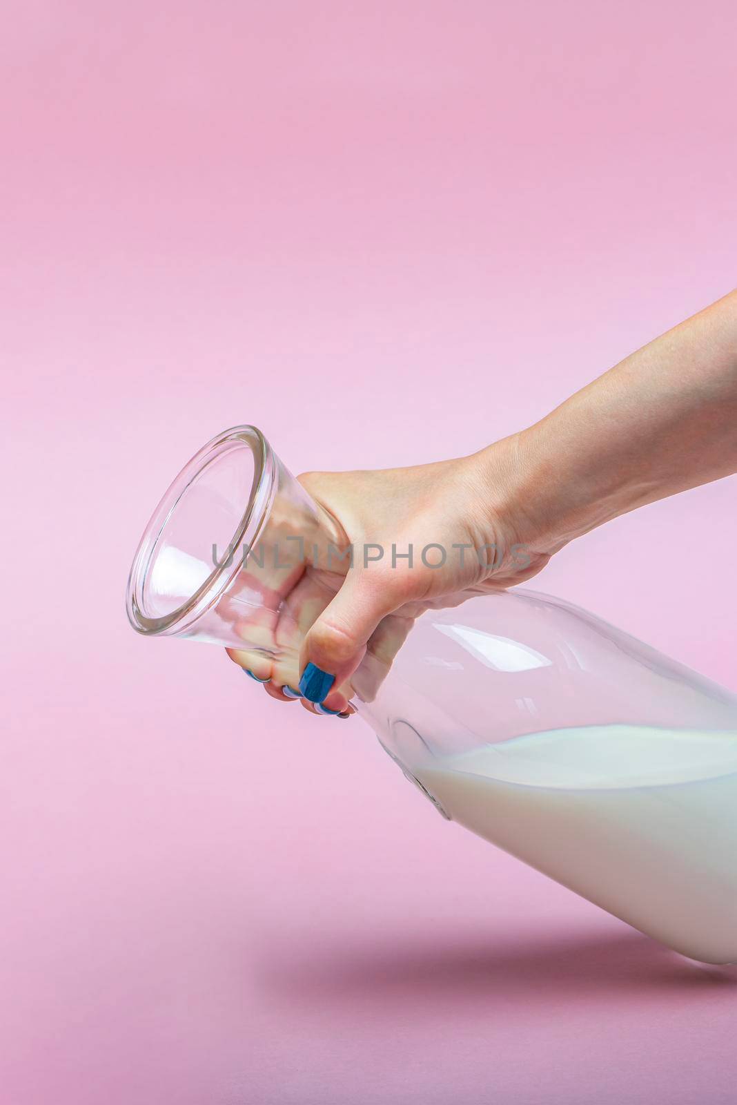 A jug of milk on a pink background in a woman's hand. Milk in a glass bottle. Space for text, large banner
