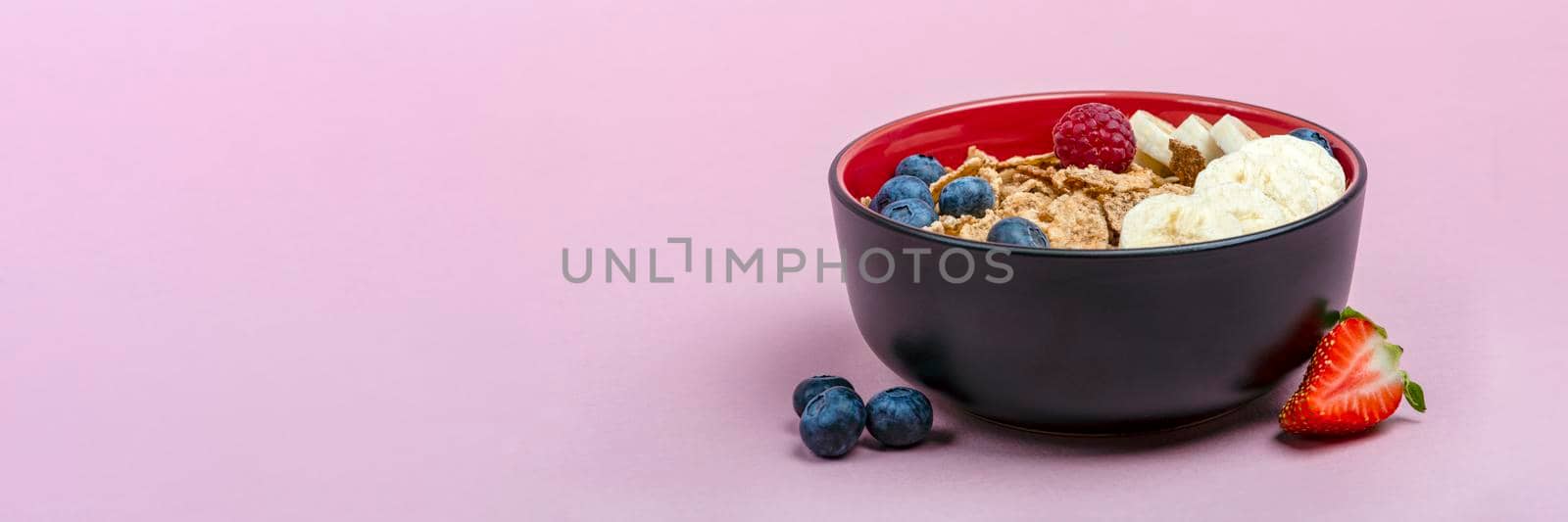 Muesli. Breakfast, healthy food and diet. Muesli with fruits in a plate on a pink background. Blueberries, strawberries and raspberries on a background of muesli flakes. Print banner with copy space.