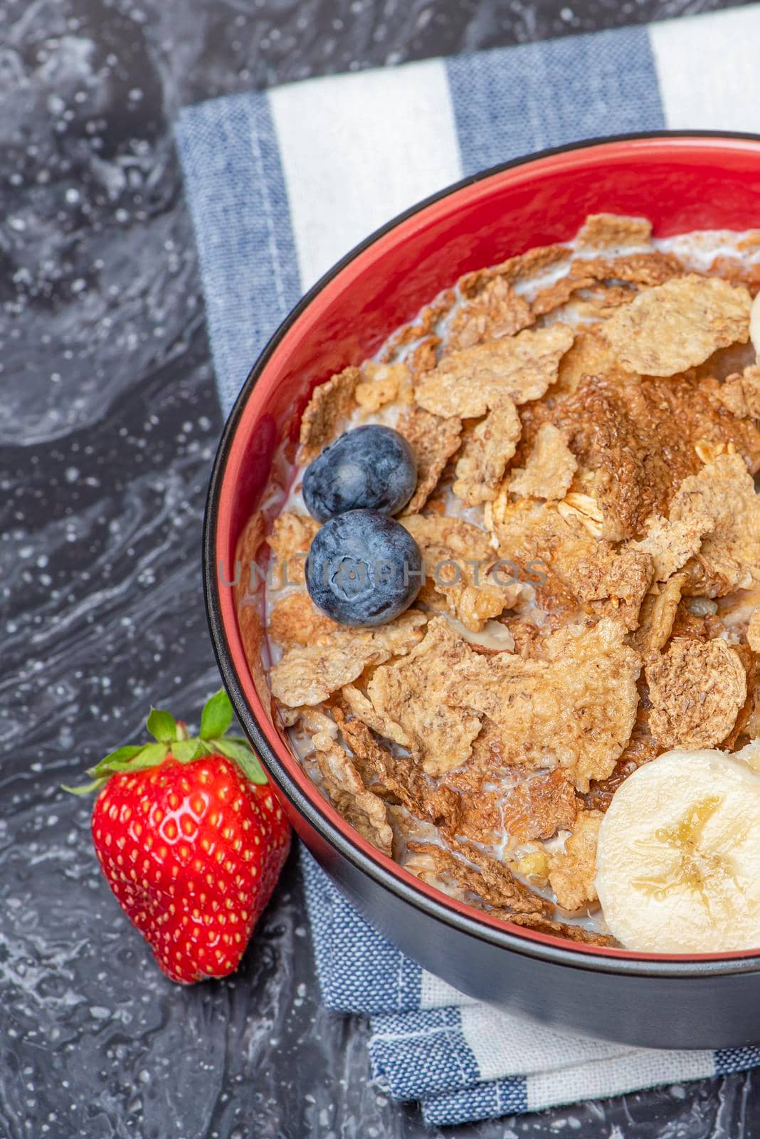 Muesli. Breakfast, healthy food and diet. Muesli with milk and fruit in a plate on a black marble top. Woman's hand with a spoon.