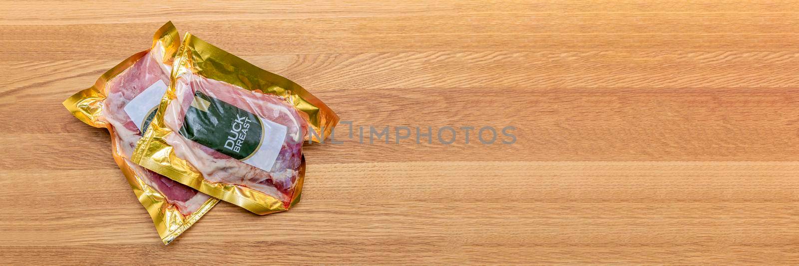 Vacuum packed duck breast. Duck meat in vacuum plastic packaging on a wooden cutting board, background for a culinary theme, place for text by SERSOL