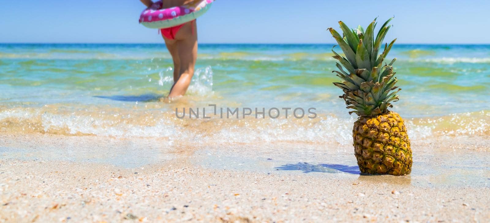 Pineapple on the beach with child going in water sea. Pineapple fruit by igor010