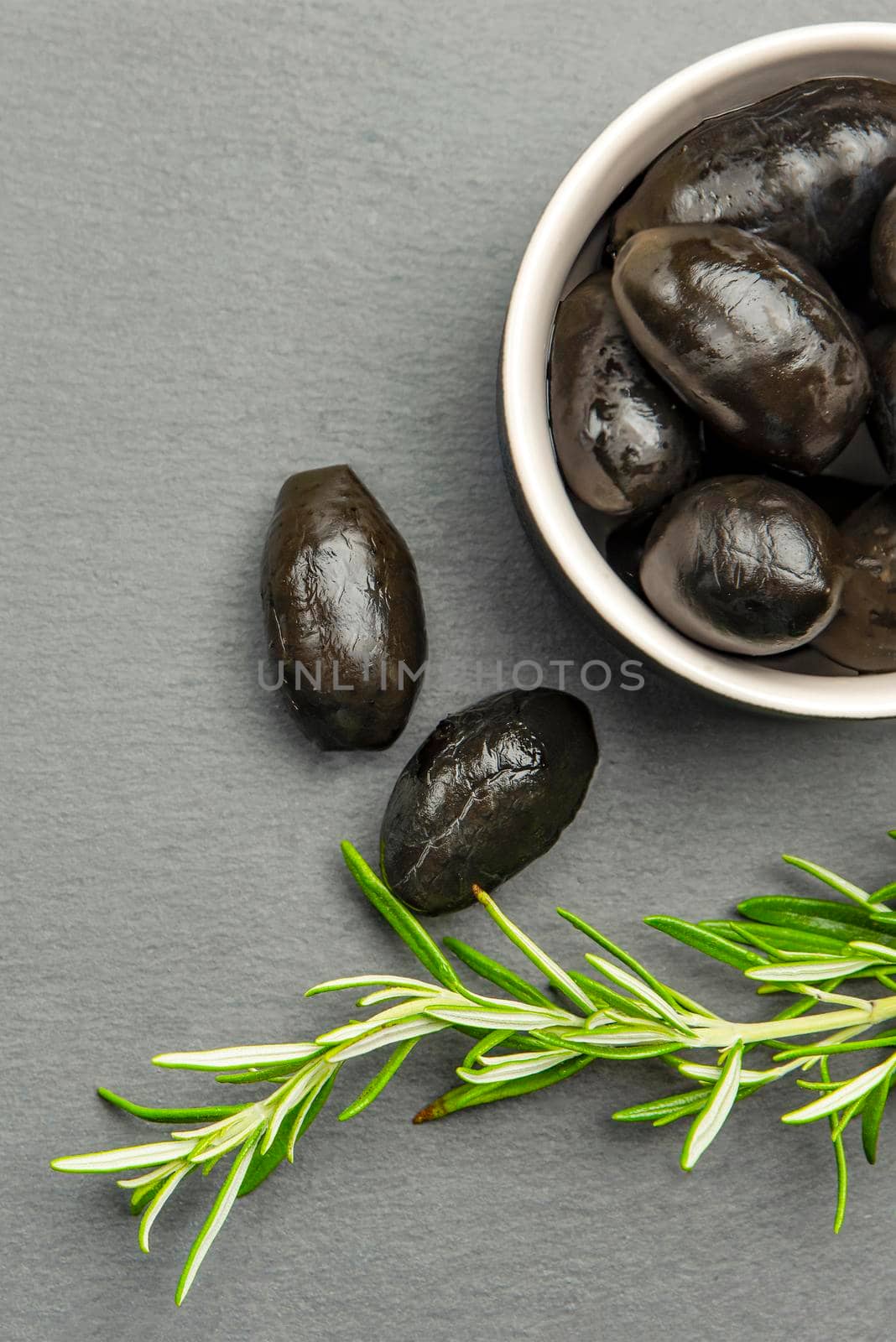 Black olives. Bella di cerignola Italian olives. Colored olives and a sprig of rosemary lie on a black stone countertop. Culinary banner or poster for advertising with place for text by SERSOL