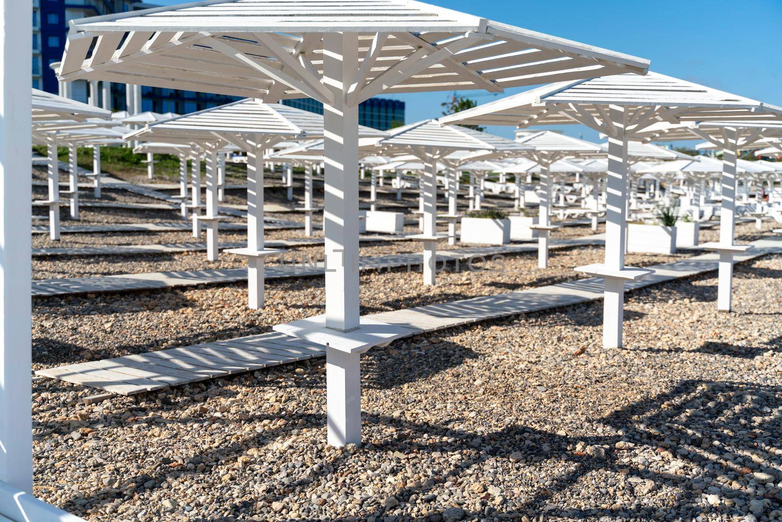 Rows of wooden umbrellas from the sun on the seashore in the morning. Wooden paths on the sand between umbrellas. Beach holiday at the resort