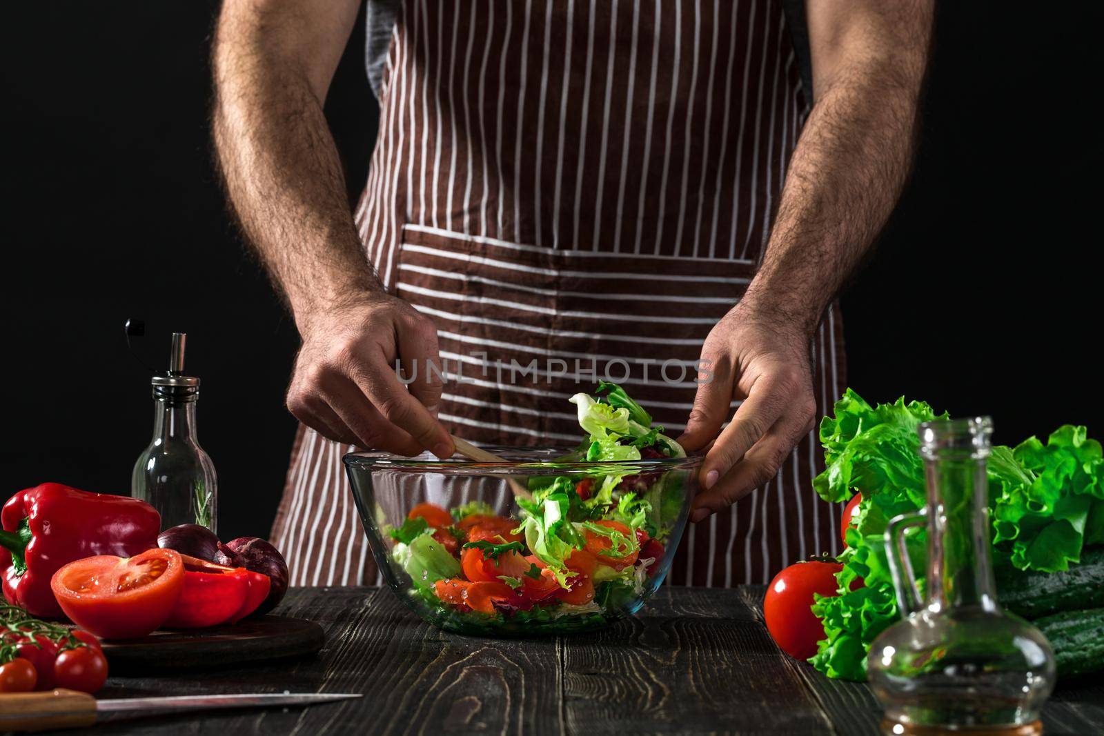 Man preparing salad with fresh vegetables on a wooden table. Cooking tasty and healthy food. On black background. Vegetarian food, healthy or cooking concept.