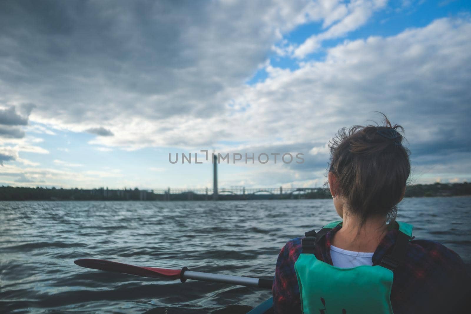 Woman exploring by the river. Young woman on kayak in the sea with blue sky and clouds on background.