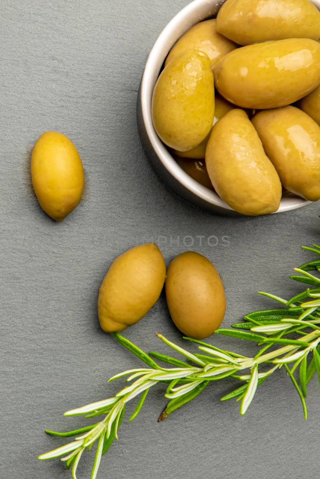 Green olives. Bella di cerignola Italian olives. Colored olives and a sprig of rosemary lie on a black stone countertop. Culinary banner or poster for advertising with place for text by SERSOL