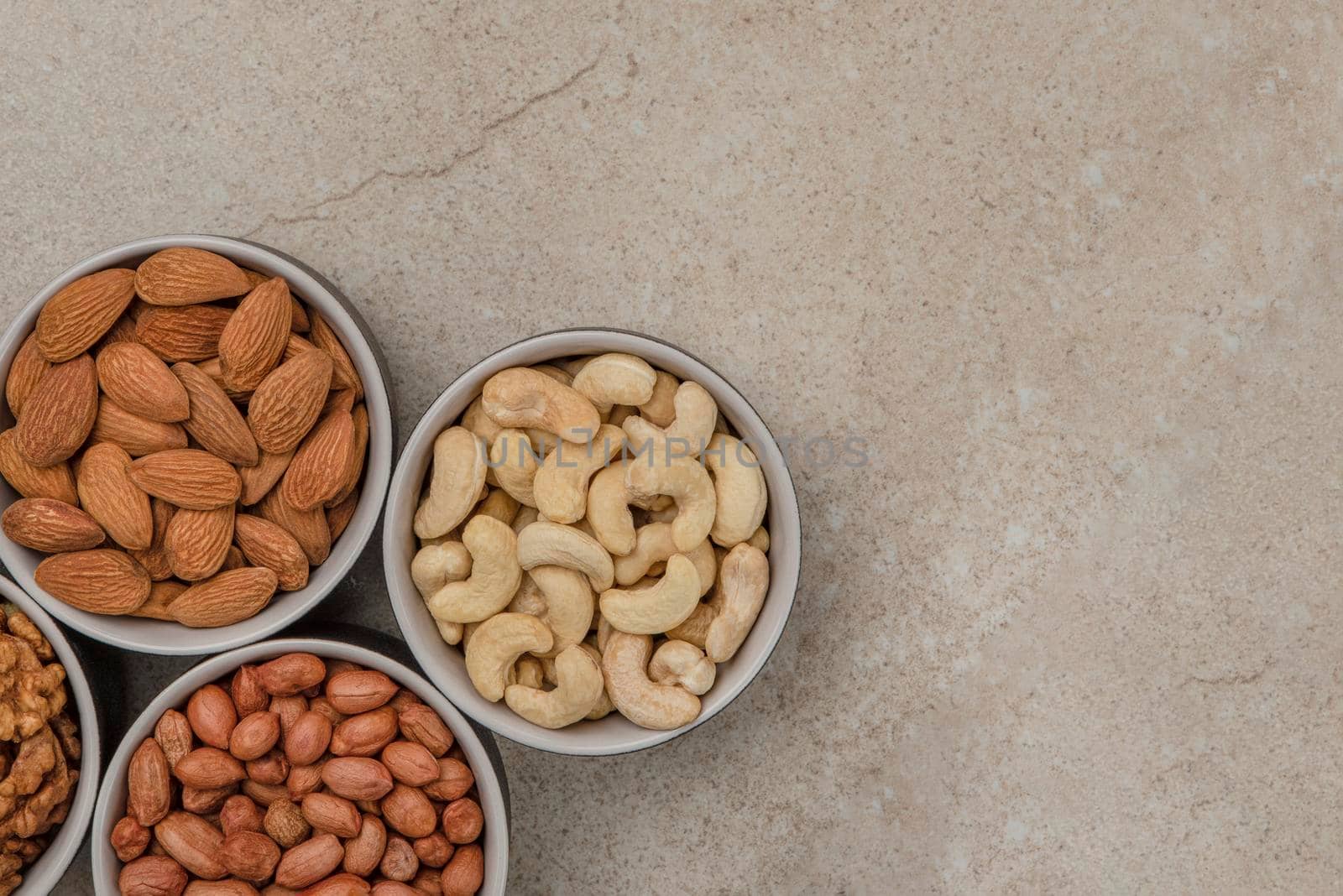 Peanuts and almonds in cups on a marble table top, top view. Superfoods and healthy eating concept.