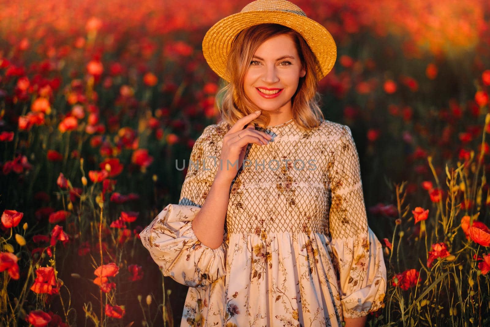 a girl in a dress, in a hat walks in a field with poppies at sunset.