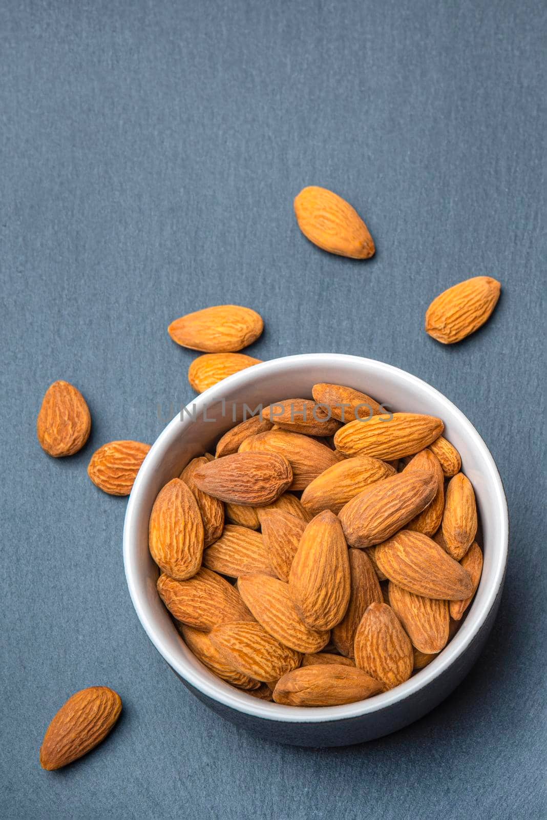 Almonds in a saucer on a black stone table top. Almonds are scattered on the table. Copy space, banner for printing.