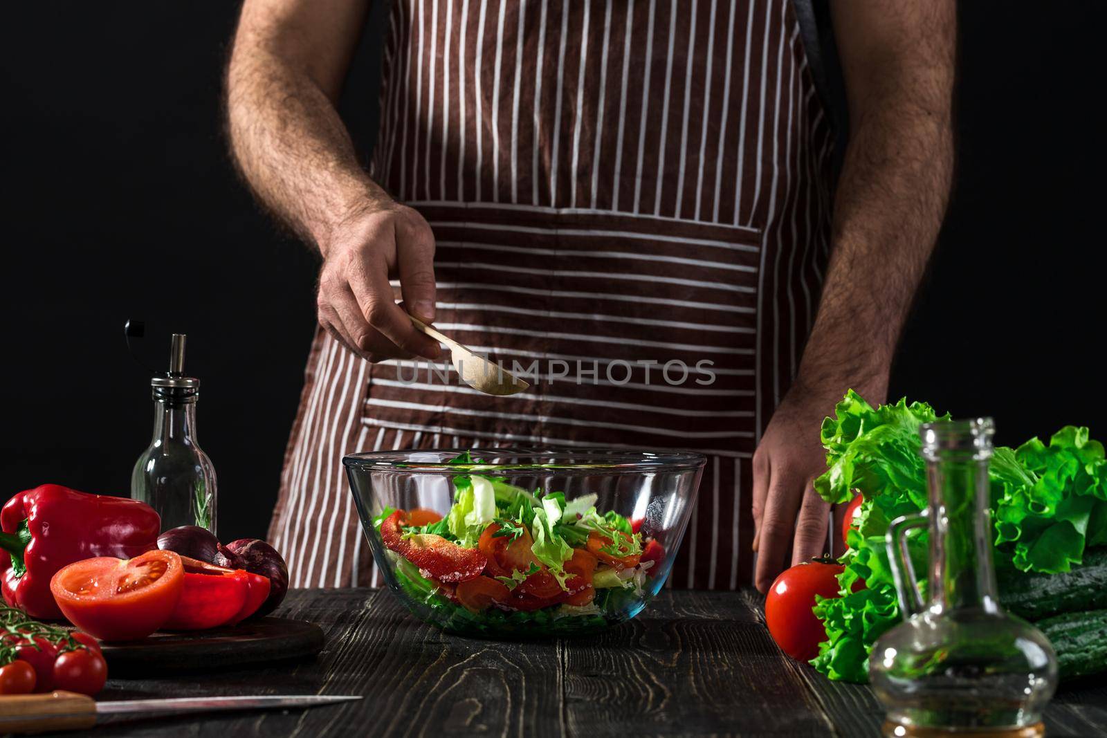 Man preparing salad with fresh vegetables on a wooden table. Cooking tasty and healthy food. On black background. Vegetarian food, healthy or cooking concept.