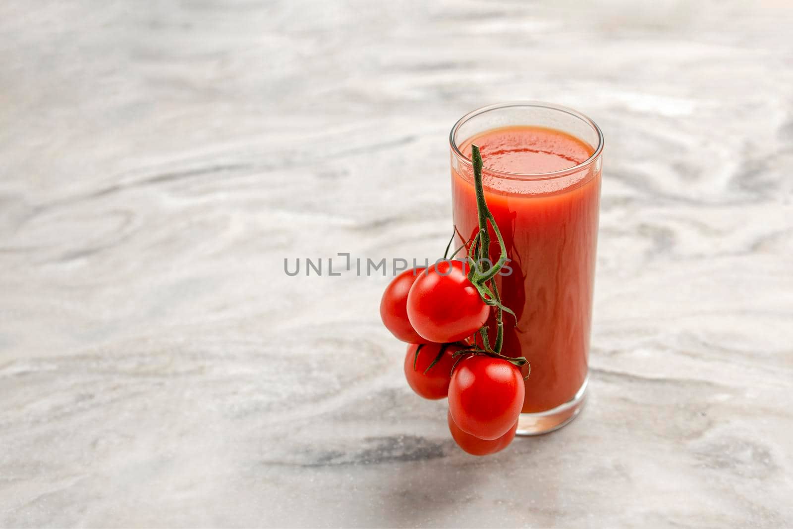 A glass of tomato juice and a branch of small tomatoes. Cherry tomatoes in a red plate on a marble background. Place to insert text or design