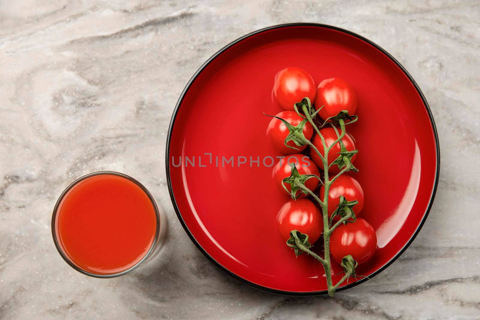 A glass of tomato juice and a branch of small tomatoes. Cherry tomatoes in a red plate on a marble background. Place to insert text or design
