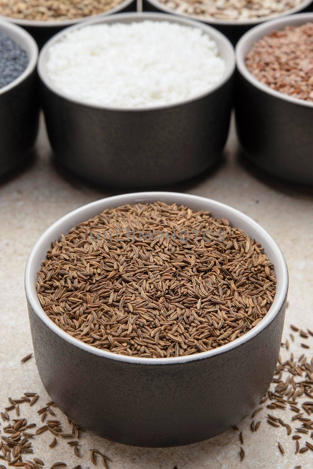 Caraway seeds. Cup with caraway seeds on a background of various seeds in black containers on a marble table top by SERSOL