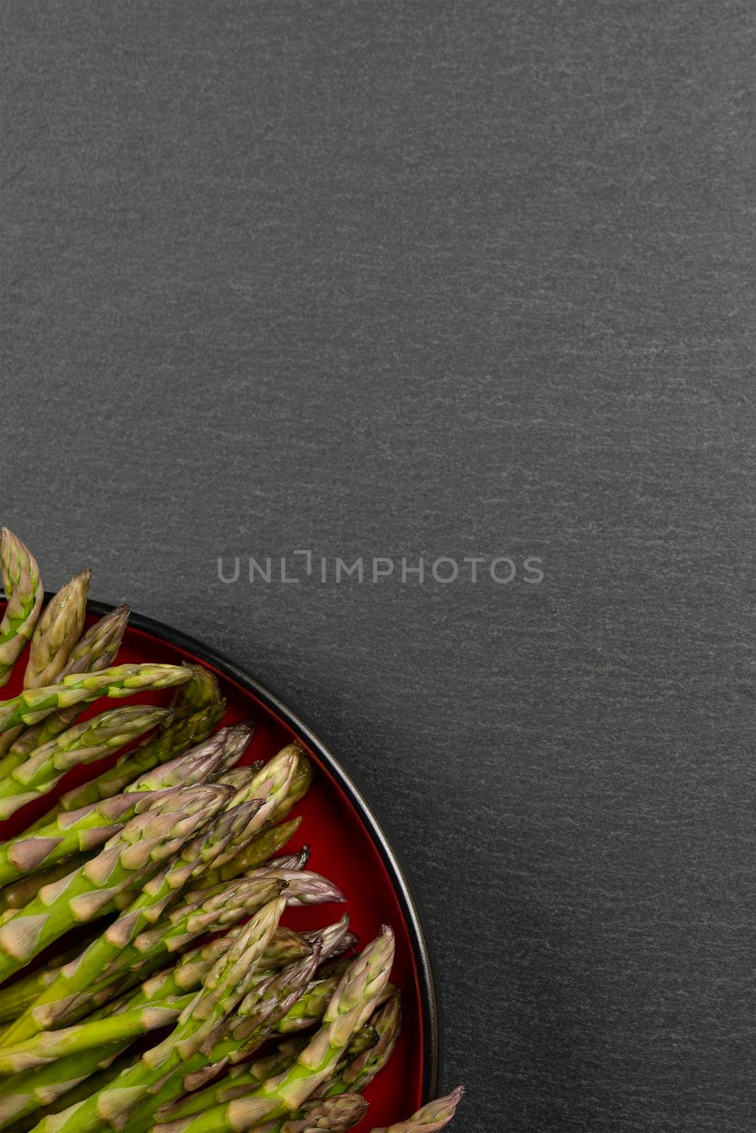 Green asparagus on a black slate stone background. Top view, asparagus in a red plate. Culinary banner with place for text