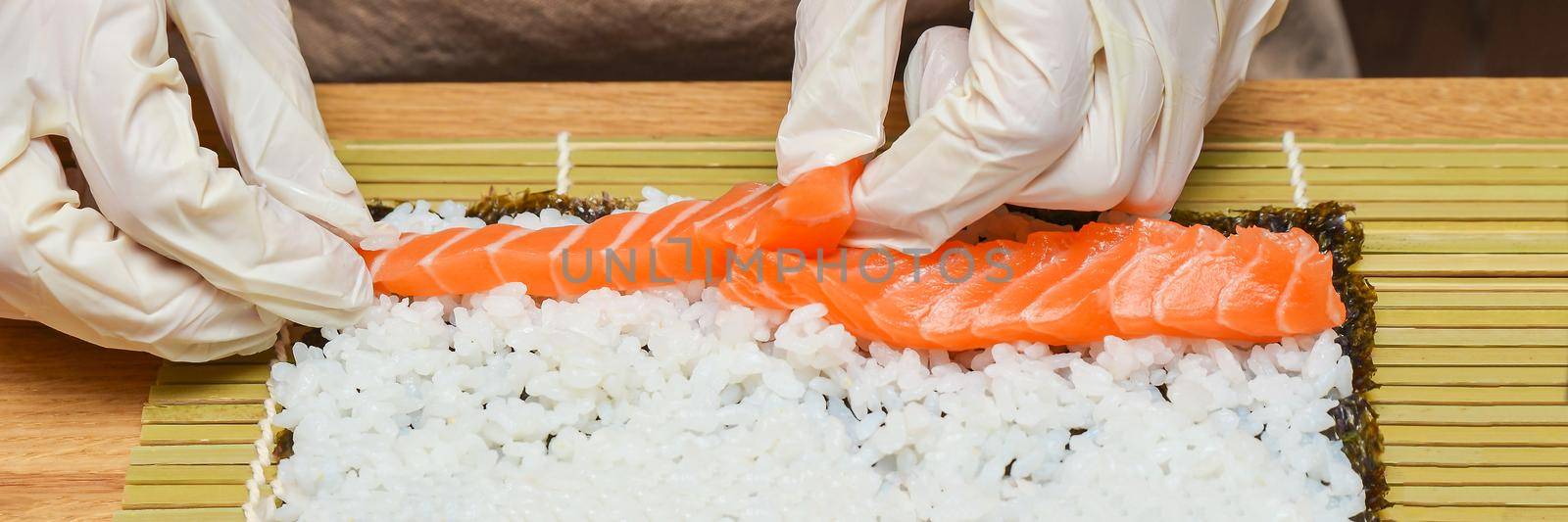 Sushi preparation process. Women's hands in rubber gloves wrap rolls for sushi, sushi at home.