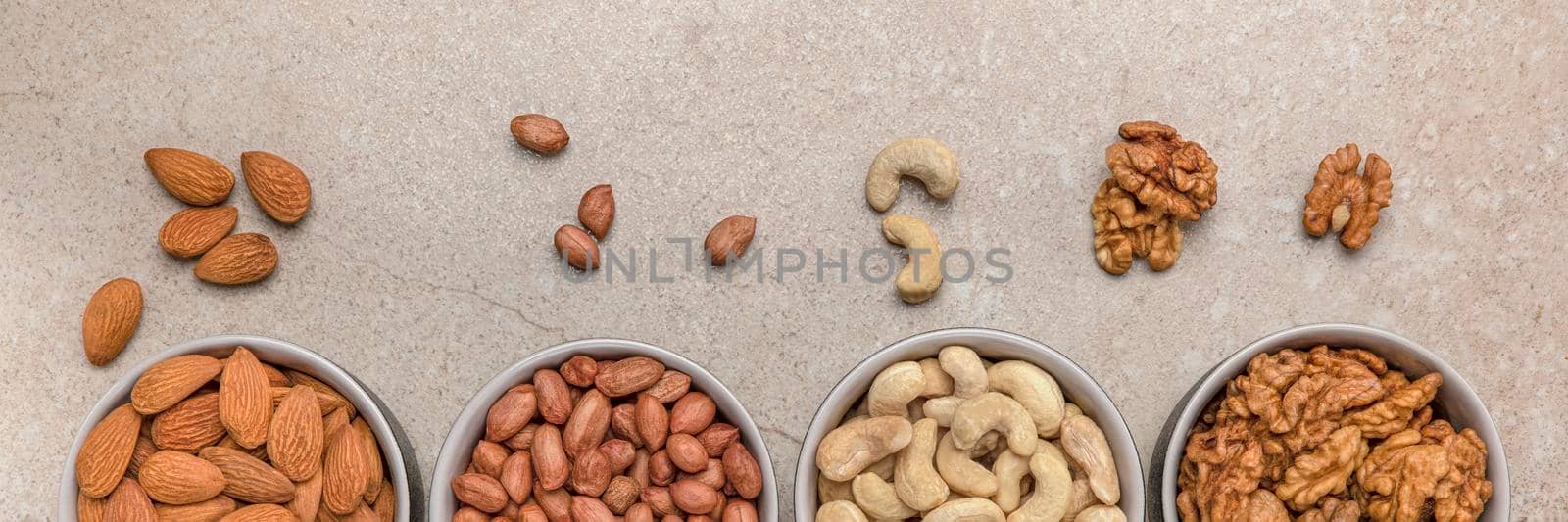 Nut background. Banner for large format printing, advertising and website design. Nuts of different varieties lie in bowls on a stone countertop, top view. Peanuts, cashews, almonds, walnuts. by SERSOL