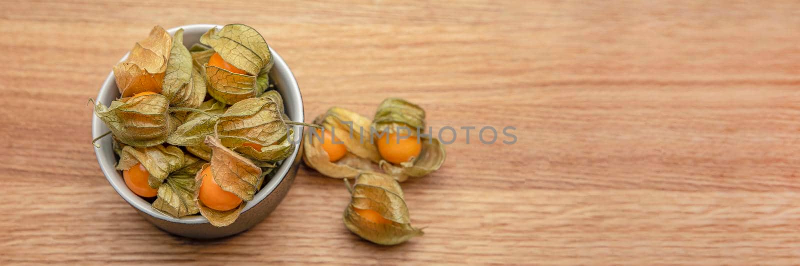 Physalis fruits on a wooden table. Sweet yellow physalis berries in a cup on wood background.