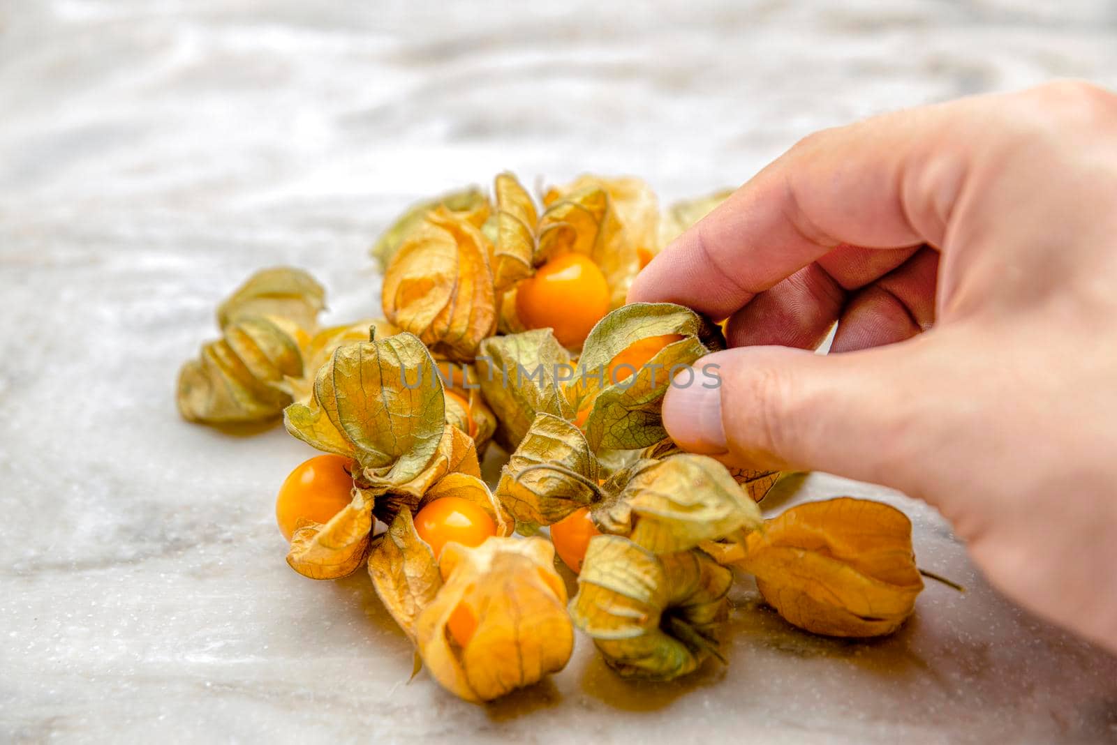Physalis in hand. The hand takes the sweet yellow physalis berries, the ripe physalis fruits lie on the marble tabletop. Place for your text , for design or product label.