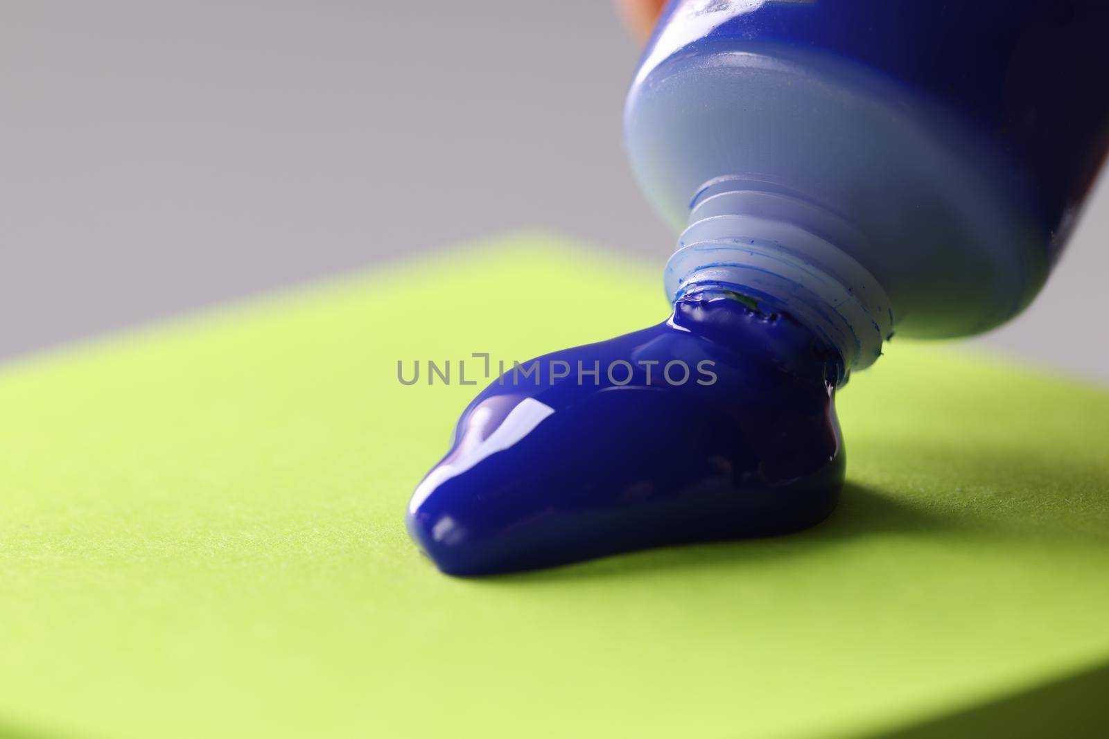 Blue paint from tube on light green sticker. Gouache tube dripping blue paint concept