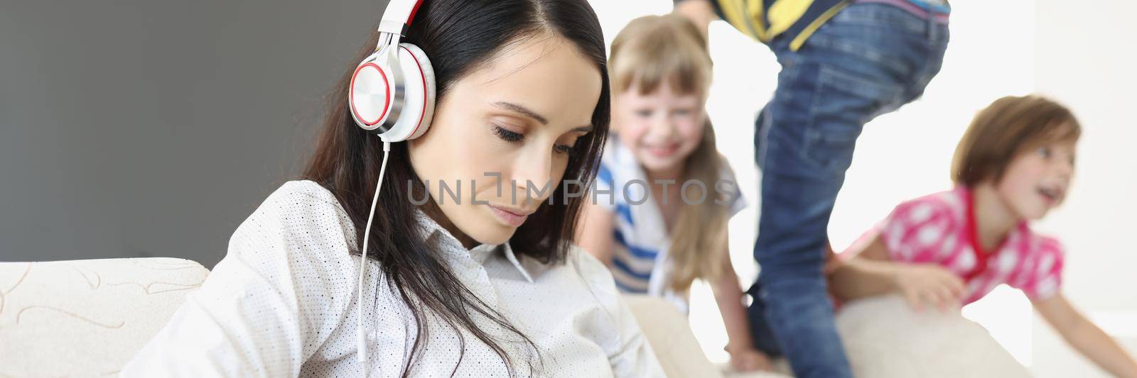 Portrait of woman trying to concentrate and work while kids going crazy and running. Mother with laptop wearing headset. Remote job, work from home, childhood, chaos, family concept