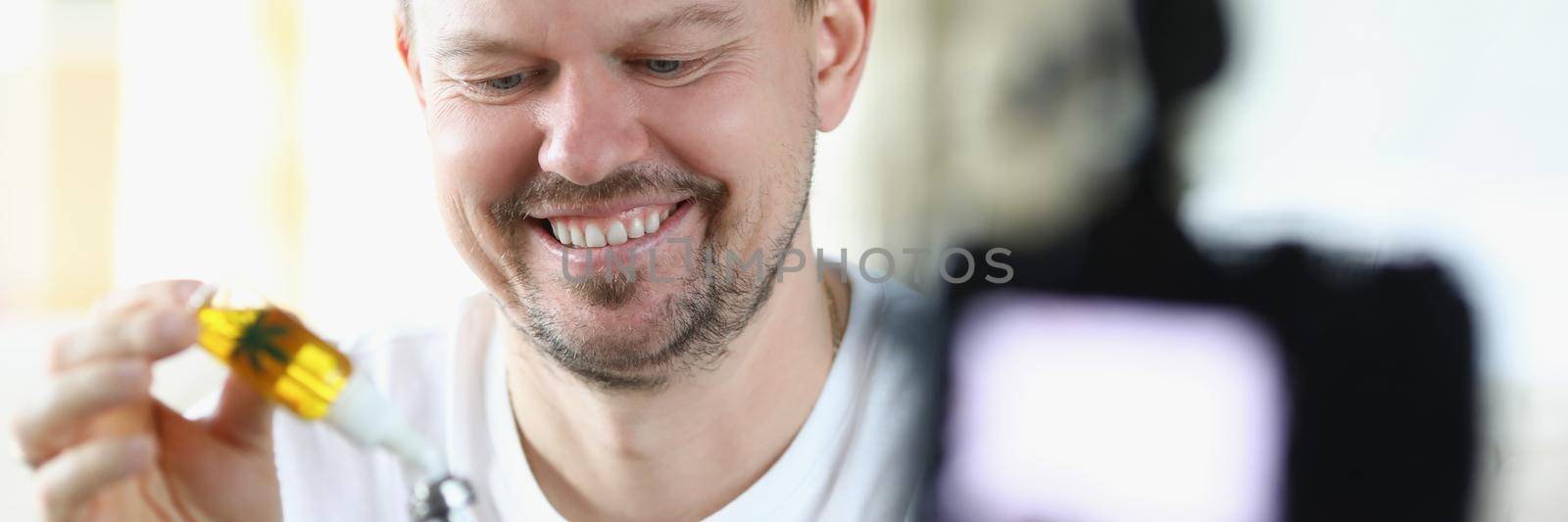 Portrait of middle aged man recording on video while he uses hemp oil. Add drop of cannabis and smiling. Video blogger, social media, technology, hobby, alternative medicine concept