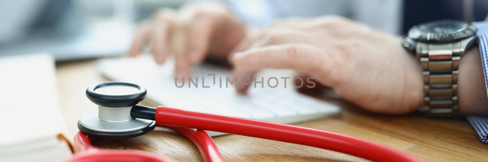 Close-up of medical equipment red stethoscope on workplace. Doctor typing on keyboard, medical building for health checkup. Medicine, clinic, appointment, healthcare concept