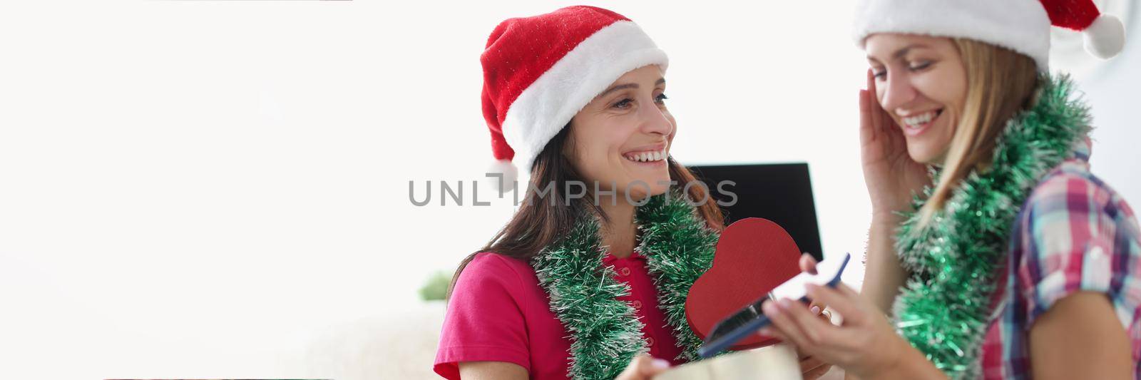 Portrait of woman giving present to sister, new model of smartphone in heart shaped box. Celebrating holiday at home, festive outfits. New year, christmas, holiday, family, sisterhood concept