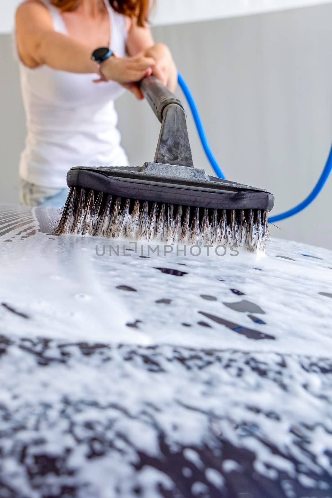 The woman washes the car. A woman at a car wash washes her car with a brush with car shampoo. To advertise a car wash or banner