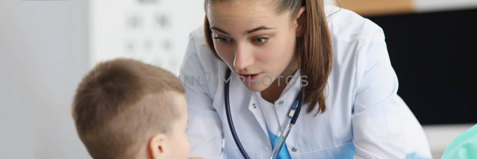 Portrait of pediatrician woman providing healthcare for kid patient in office, specialized clinic for children. Young qualified woman doctor with stethoscope. Medicine, healthcare concept