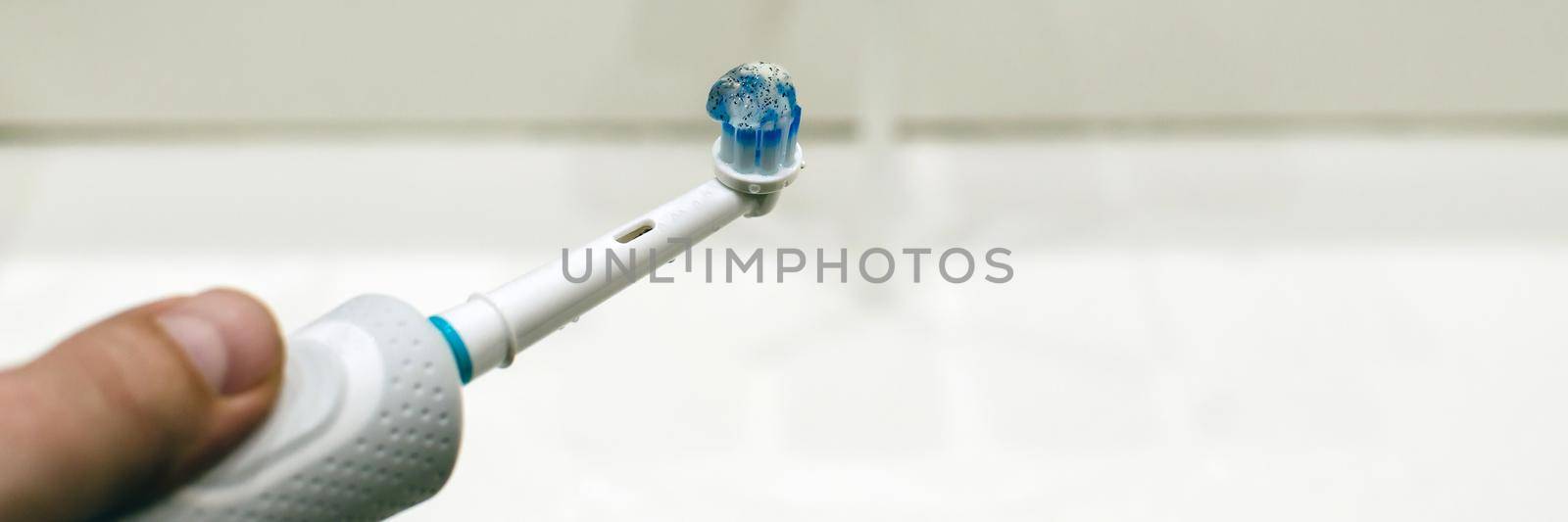 Rechargeable, electric toothbrush, close-up. Against the backdrop of a bathroom in white. Water faucet and white sink.