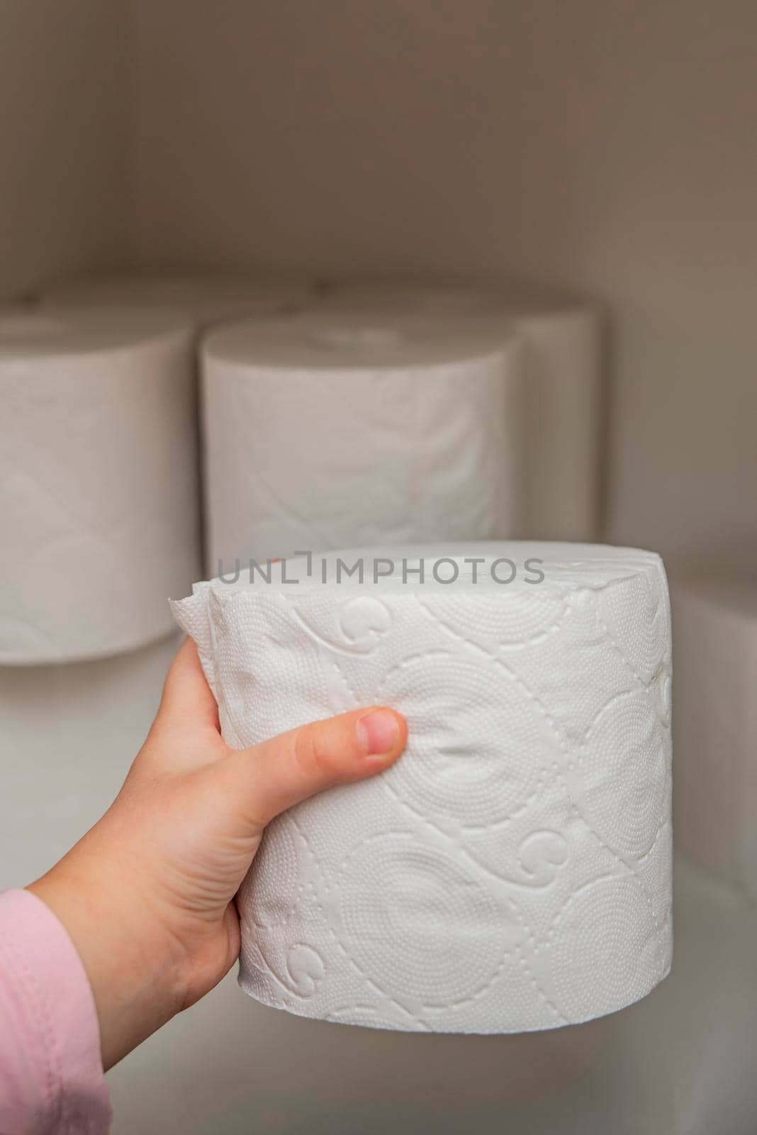 Roll of white toilet paper in hand. The child's hand takes a roll of toilet paper from the cabinet. Lots of toilet paper on background.