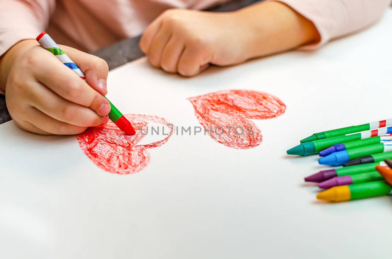 A little girl is drawing a heart with red chalk - high angle image with selective focus. Valentine's day concept.