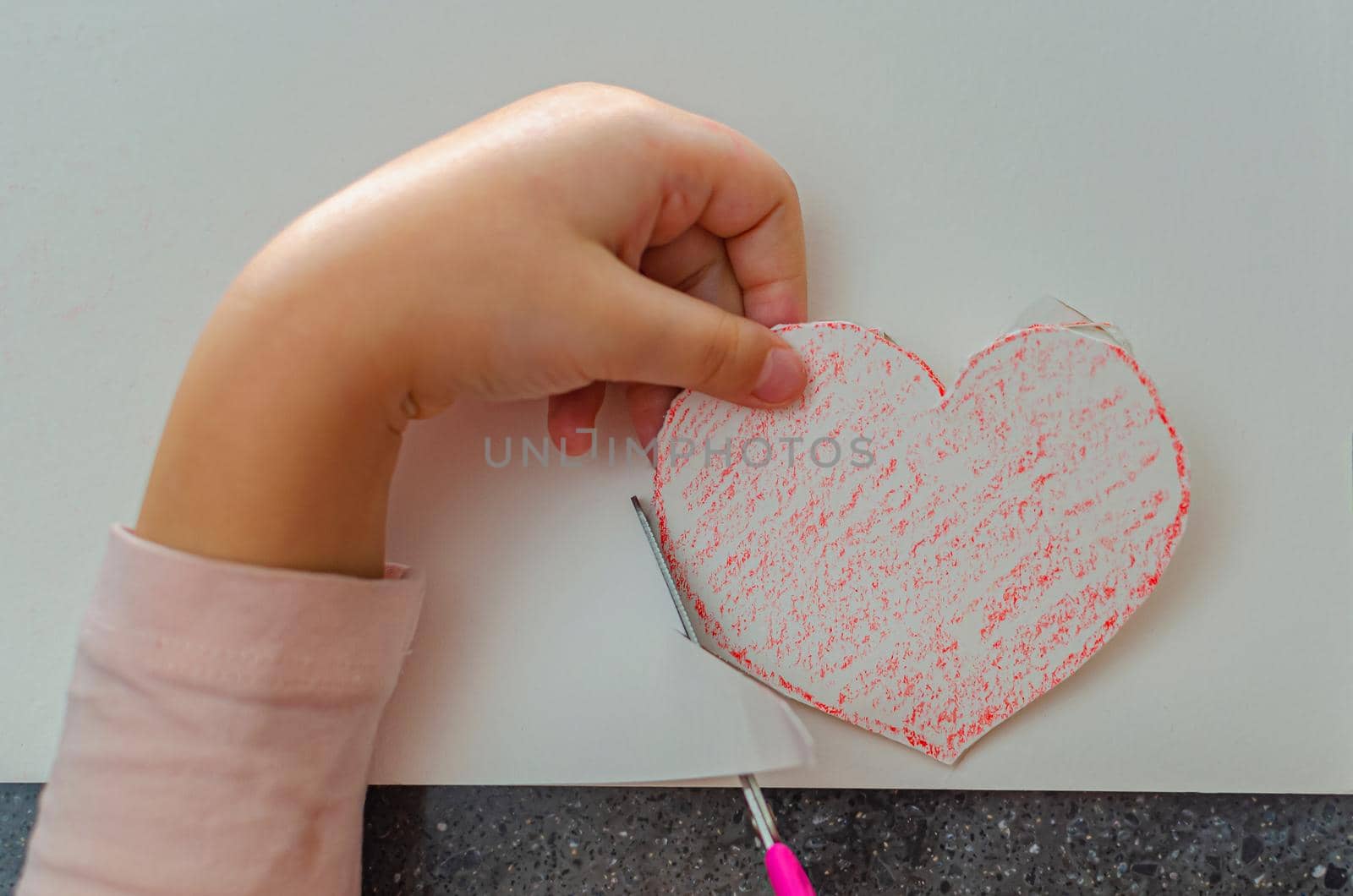 The girl's hand holds a heart cut from paper. Children's creativity - drawings and crafts for Valentine's Day or Mother's Day